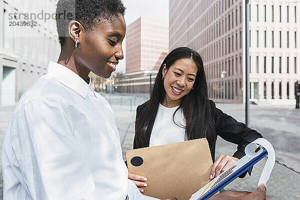 Happy businesswomen discussing over clipboard at office park