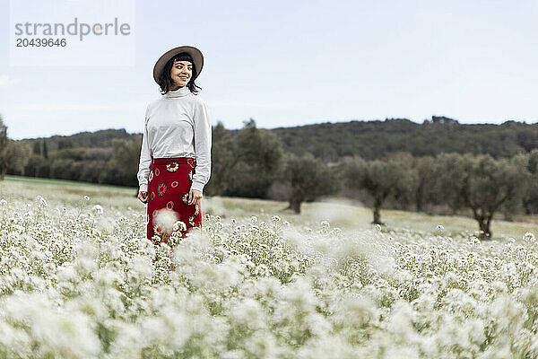 Smiling young beautiful woman standing amidst white flowers in field