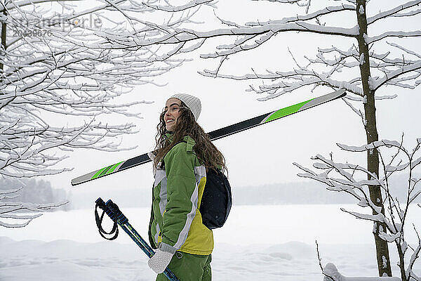 Cheerful woman wearing ski Jacket and standing in winter forest