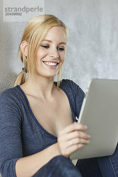 Smiling young woman using tablet PC and leaning on wall