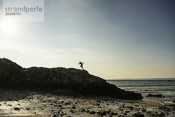 Man running over rock near sea at sunset