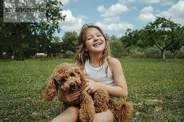 Cheerful girl sitting with Maltipoo dog in farm