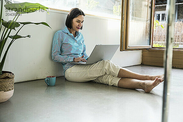 Smiling mature businesswoman sitting using laptop in office