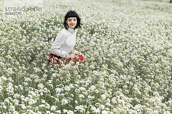 Young beautiful woman squatting amidst white flowers at field