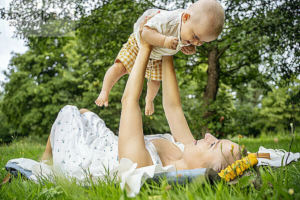 Mother lying on grass holding aloft cute baby in garden