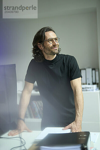 Smiling mature businessman leaning on desk at office