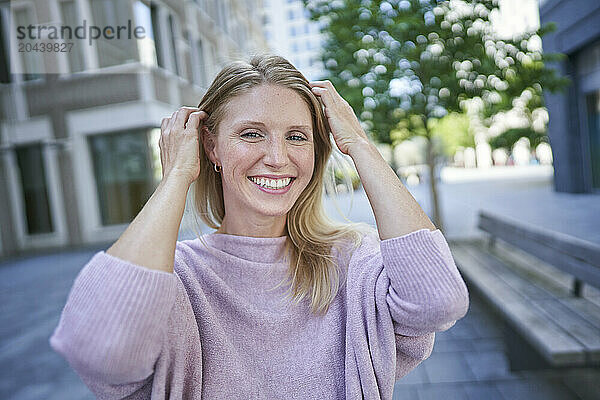 Happy woman with hand in hair standing near building