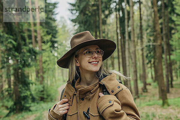 Smiling woman wearing eyeglasses and hat in forest