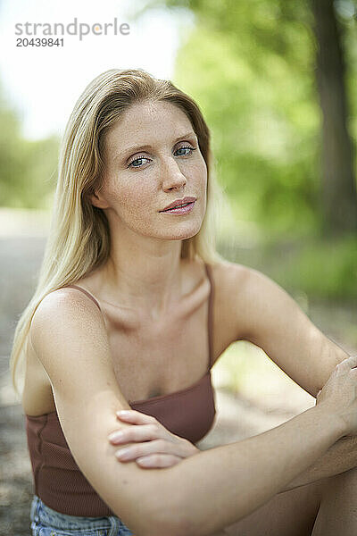 Blond hair woman sitting on ground with arms crossed at forest