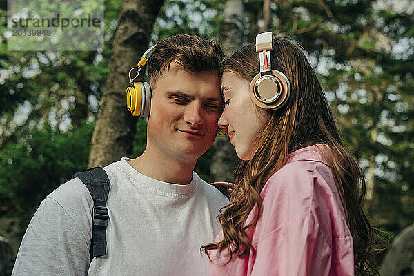 Happy young couple wearing wireless headphones listening to music and embracing each other