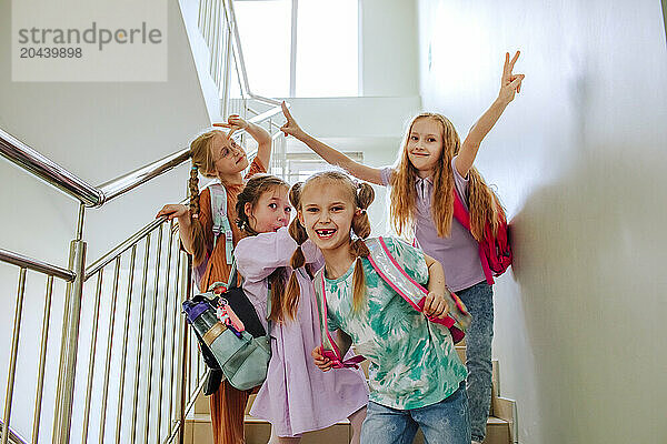 Happy schoolgirls with hand raised standing on school staircase