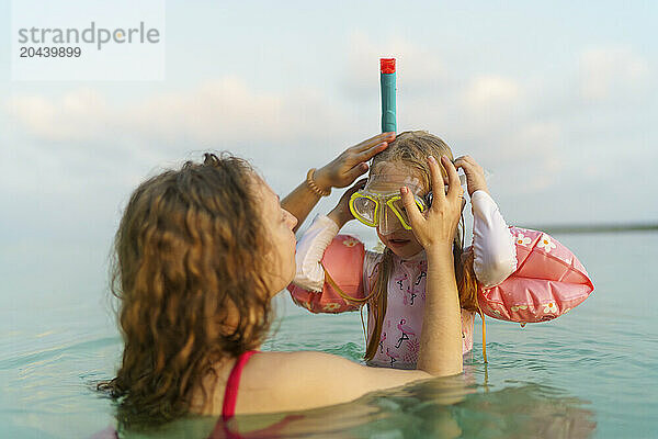 Mother and daughter snorkeling together in sea at sunset