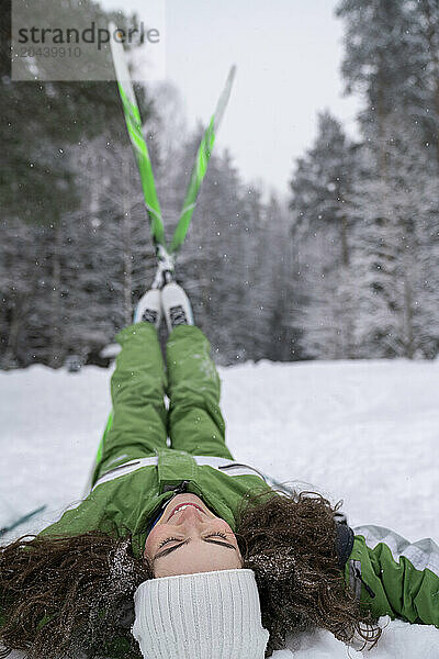 Young woman with legs in air lying on snow at winter forest