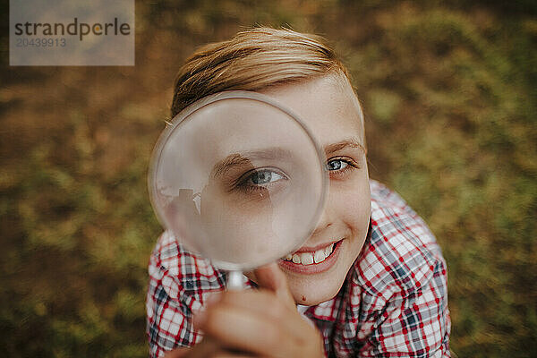 Smiling blond boy with magnifying glass in garden