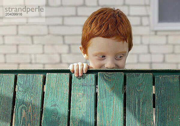 Redhead boy behind green planks