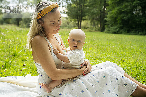 Cute baby sitting on lap of mother in garden