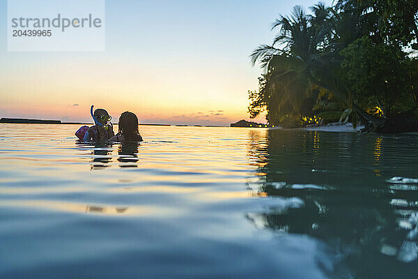 Mother and daughter snorkeling in sea at sunset