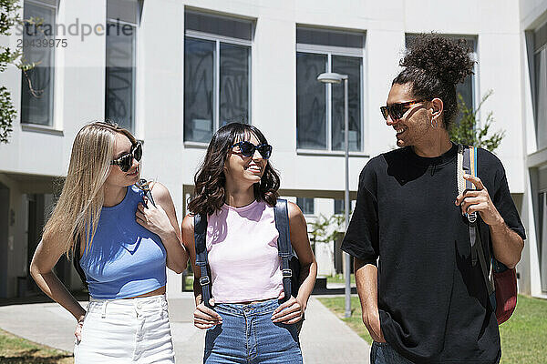 Happy friends wearing sunglasses talking at university campus