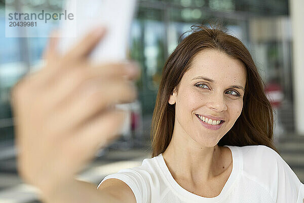 Smiling woman taking selfie through smart phone at airport