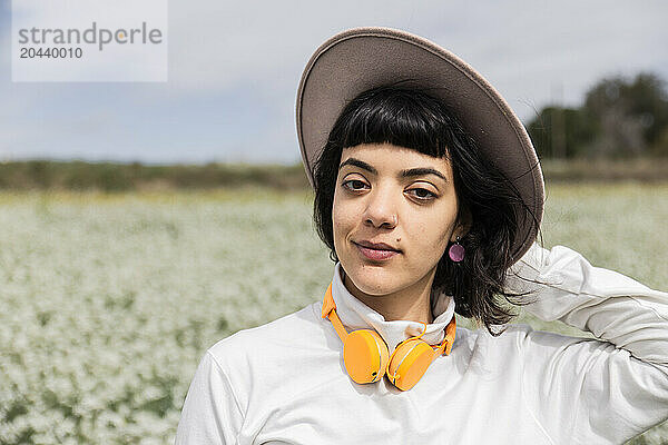 Beautiful young woman with headphones wearing hat at field