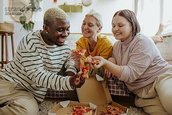 Happy young friends enjoying pizza at home