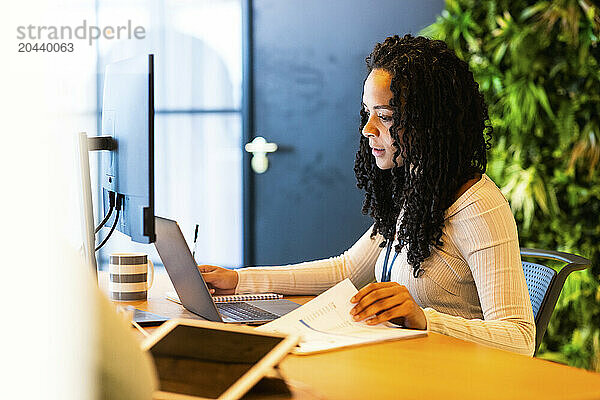 Businesswoman with curly hair working on laptop at coworking space