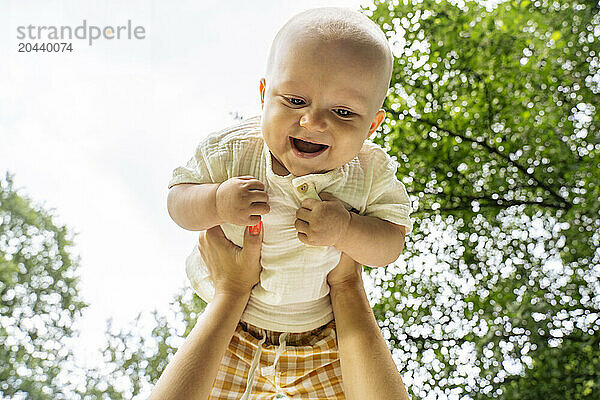 Hands of mother holding aloft baby boy at park