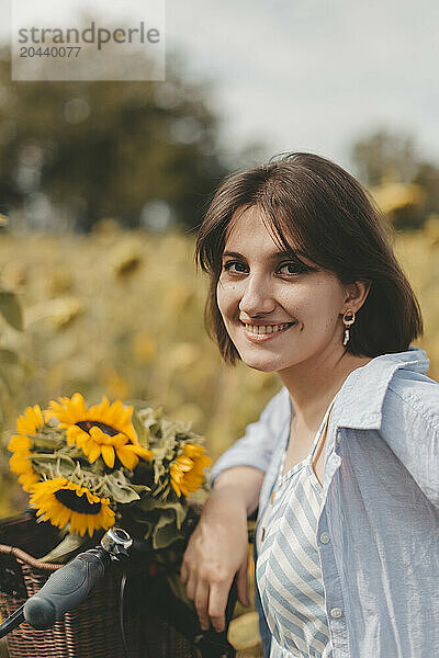 Smiling woman with sunflowers in bicycle basket at field