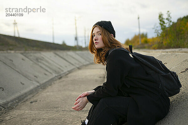 Thoughtful young hibster woman with backpack sitting in dry canal