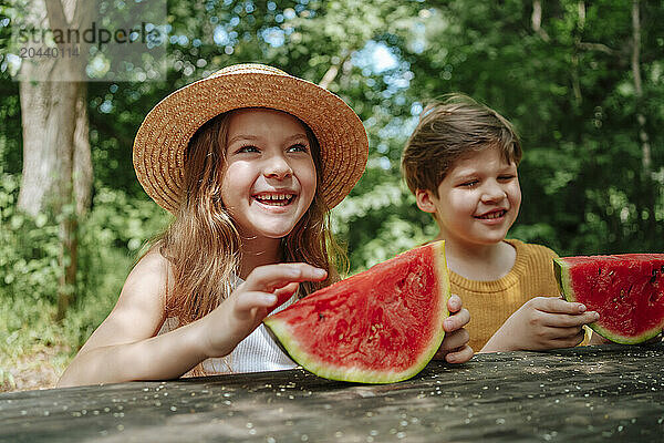 Boy and girl eating watermelon on table in summer