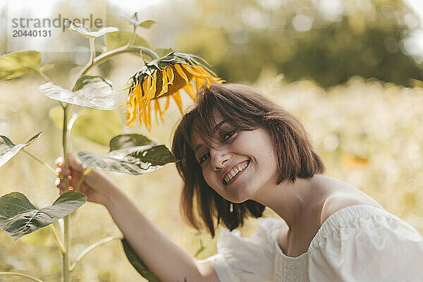 Smiling young woman holding sunflower at field