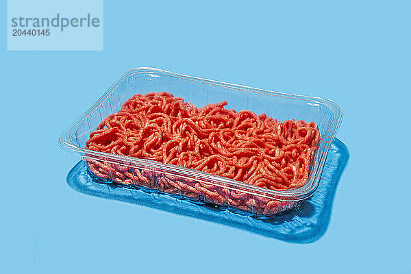 Ground beef in plastic tray against blue background