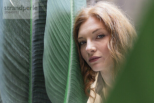 Young beautiful redhead woman leaning on leaf in city