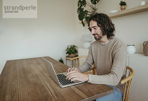 Smiling businessman using laptop at table working from home