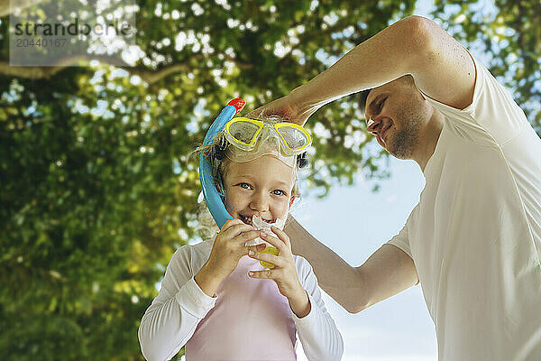 Father helping daughter with snorkel and swimming goggles