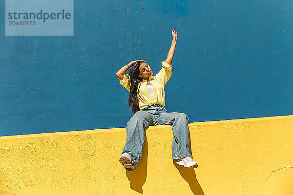 Young woman with hand raised sitting on wall