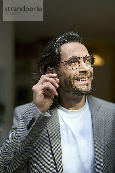 Thoughtful smiling handsome businessman wearing eyeglasses at office