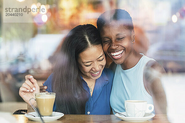 Happy friends drinking coffee sitting at table in cafe