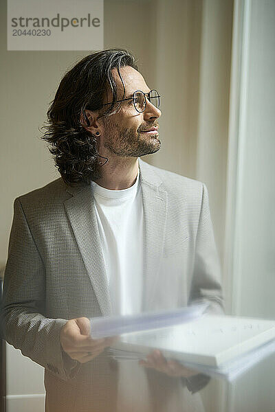 Thoughtful businessman standing with document at office