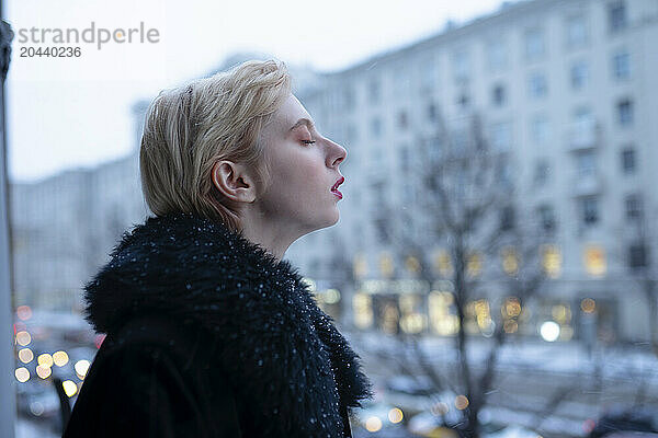 Blond woman wearing fur coat and standing with eyes closed