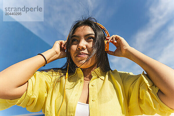 Woman listening to music with headphones in front of sky