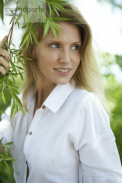 Beautiful woman wearing white shirt holding branch at forest