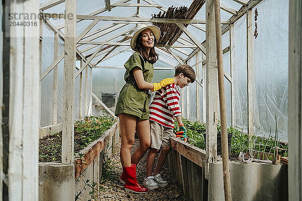 Happy mother and son standing in greenhouse