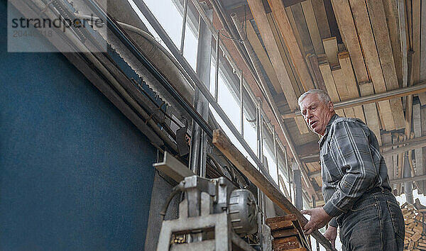 Man processing wooden plank on machine in workshop