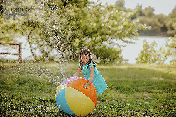 Girl playing with colorful beach ball splashing water at garden