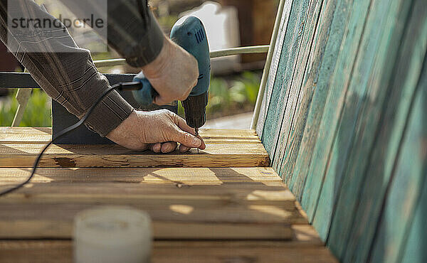 Hands of senior man using screwdriver on plank