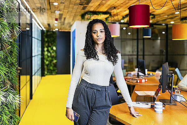 Confident businesswoman standing near desk at coworking space