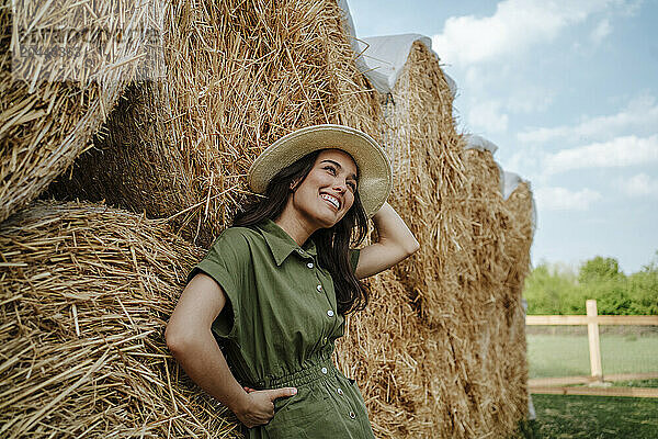 Happy young farmer leaning on haystacks at farm