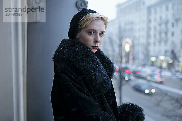 Young woman wearing fur coat and standing in balcony