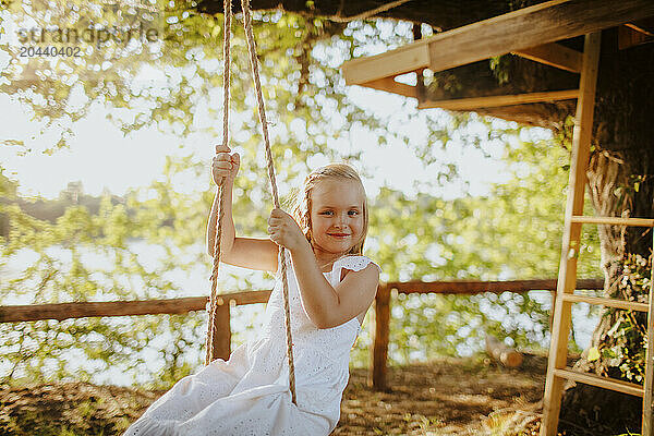 Smiling blond girl enjoying swing at garden